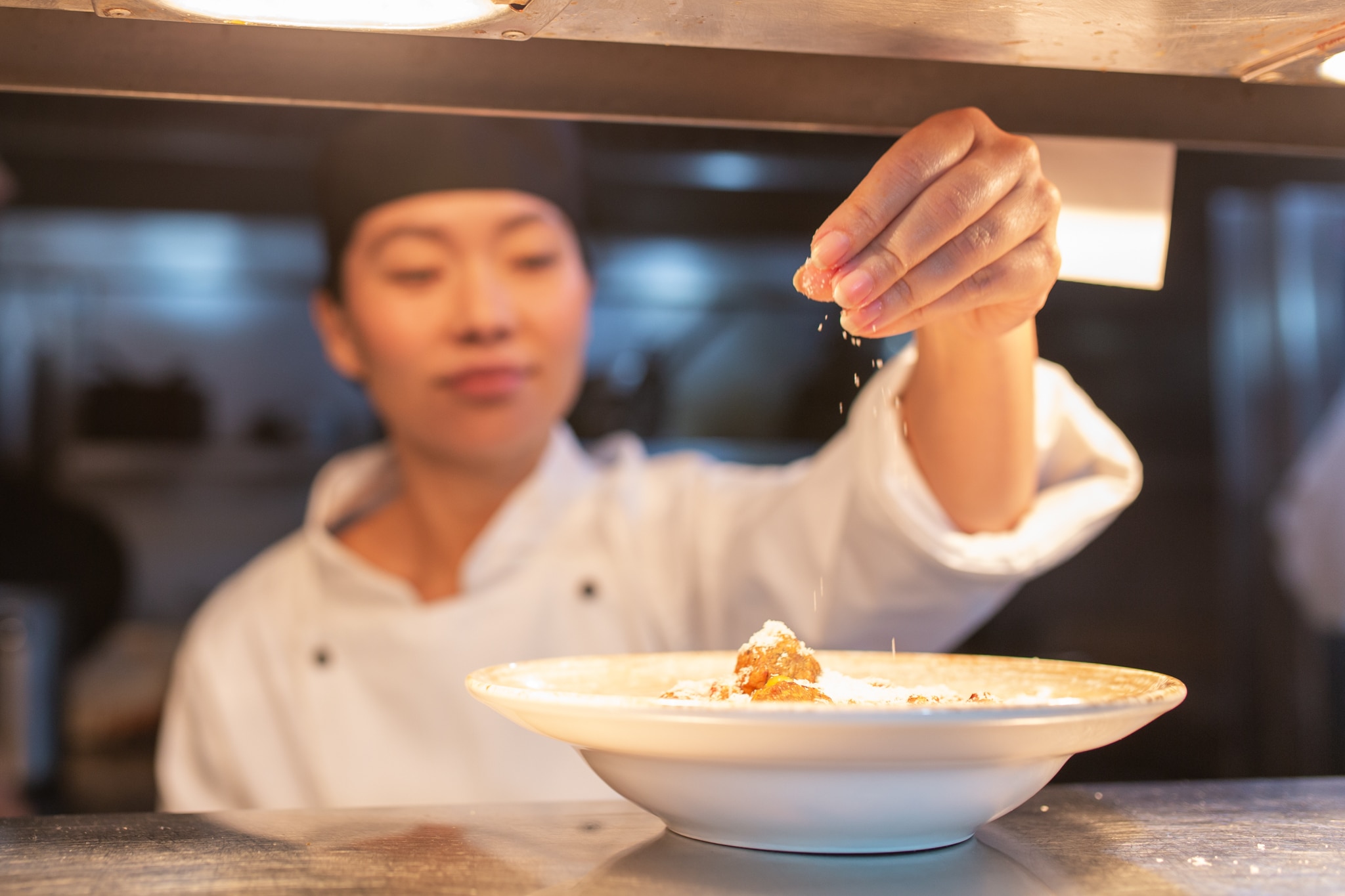 Female chef sprinkling spices on a dish in a restaurant kitchen.