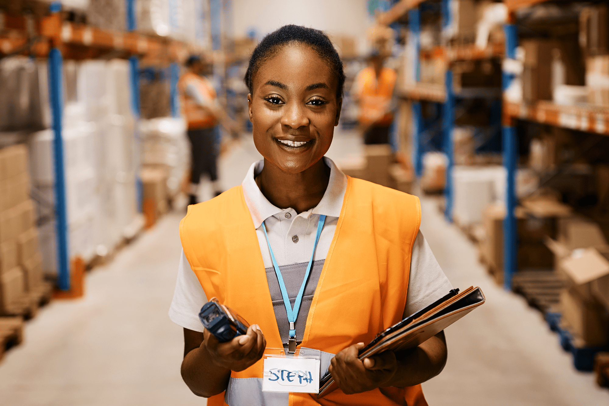 Happy female warehouse worker working at distribution warehouse and looking at camera.