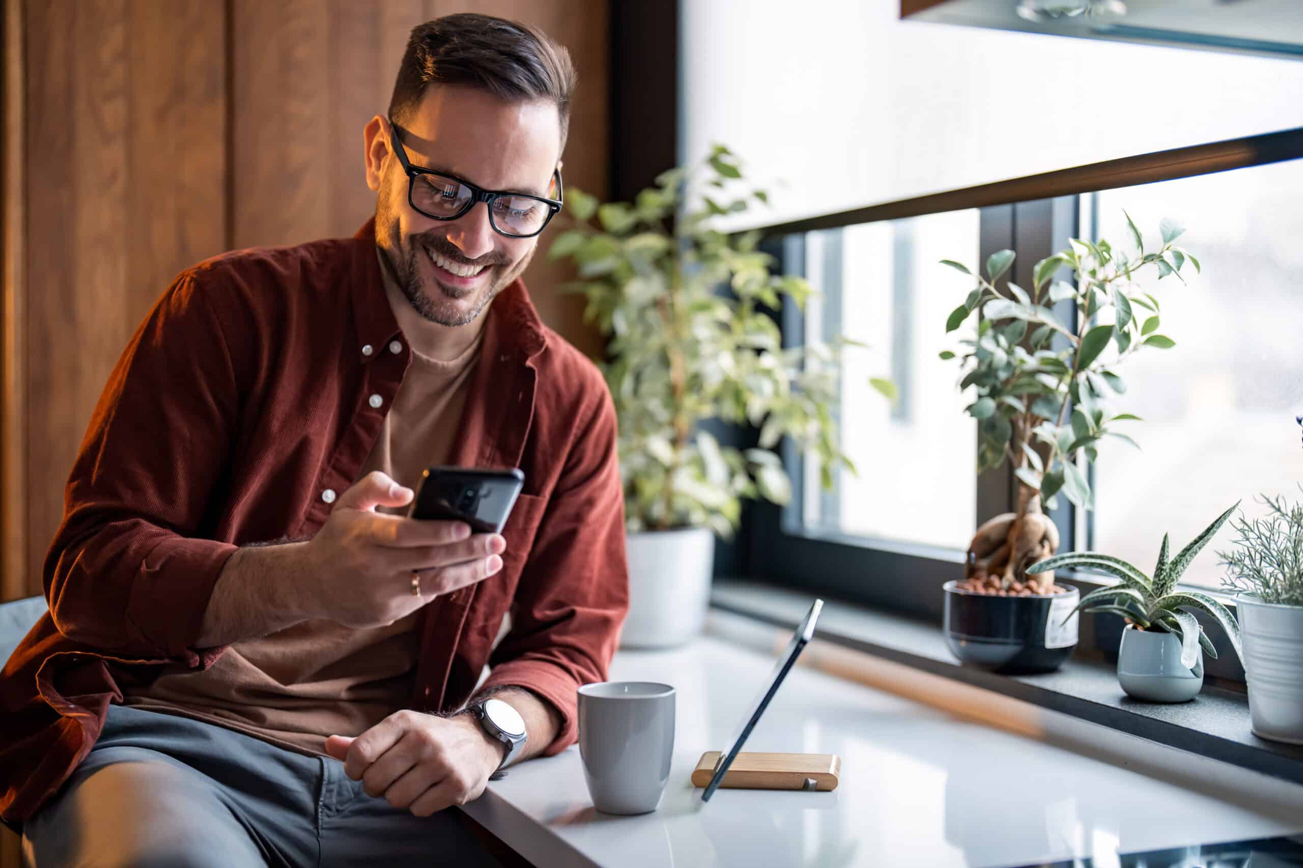 Happy handsome millennial man holding and using smartphone for typing, surfing the internet or writing text messages
