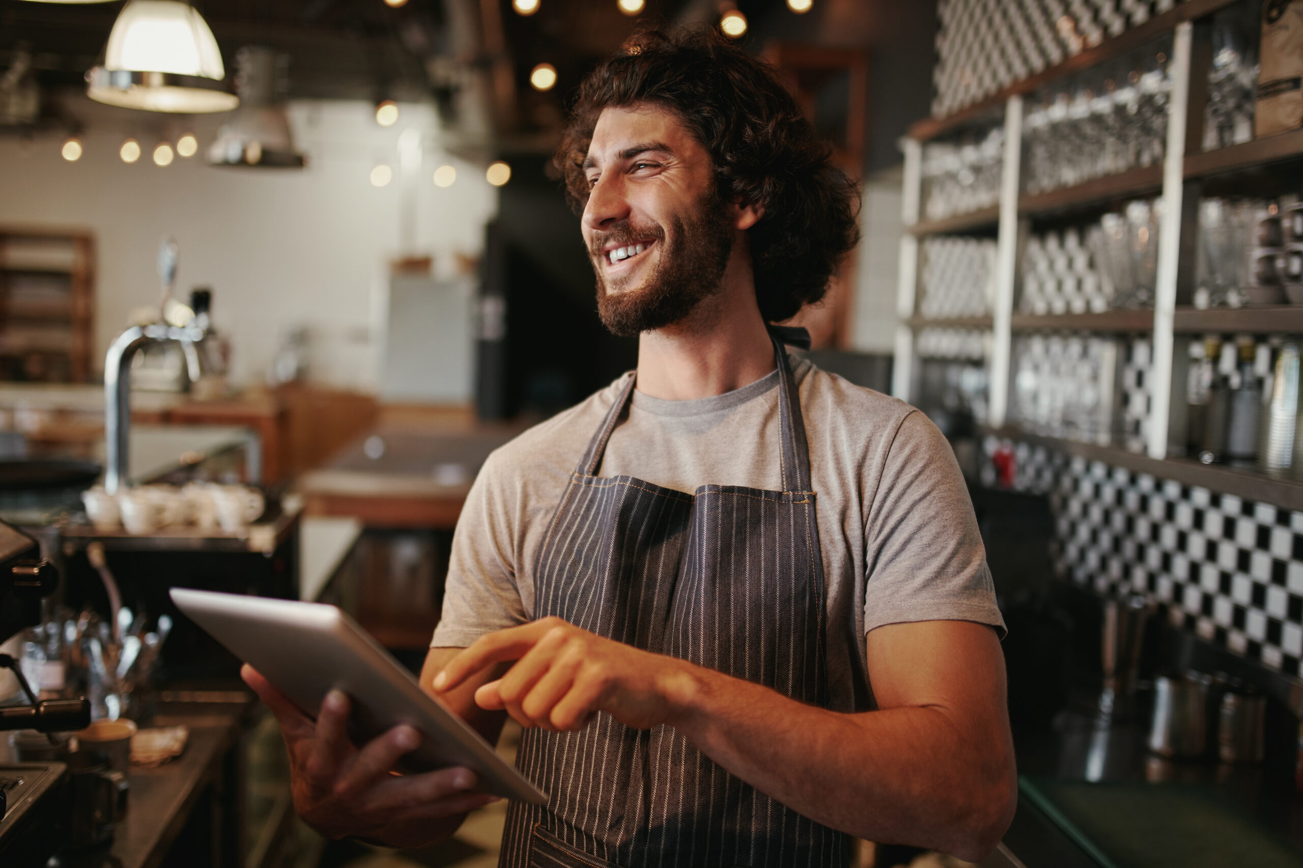 Cheerful waiter behind counter using digital tablet
