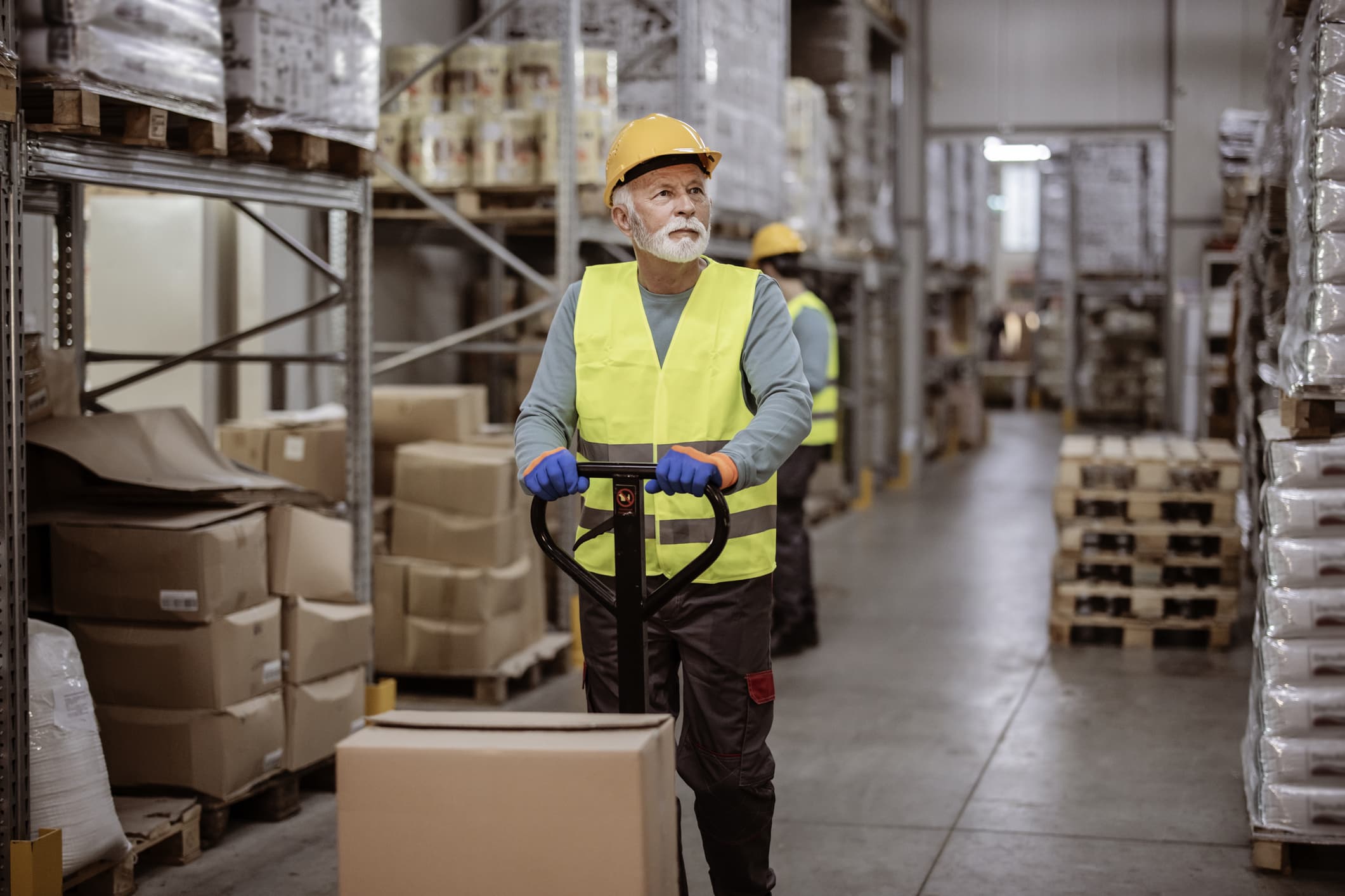 Senior male worker in uniform in the warehouse with pallet truck