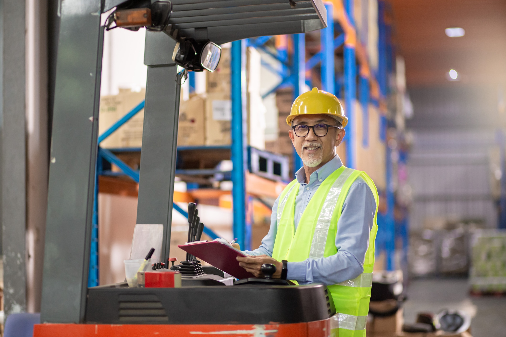 Asian Chinese senior warehouse worker operating forklift working in industry factory